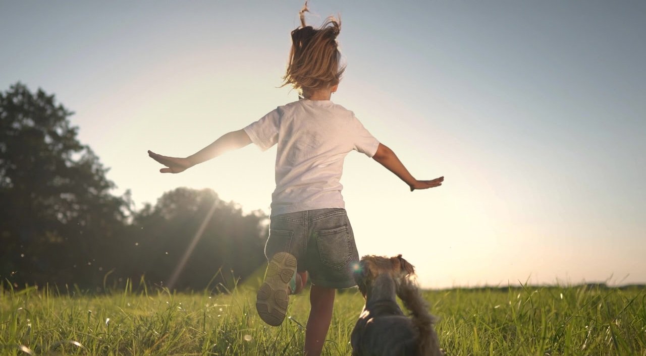 Young child running outdoors with a dog in a grassy field